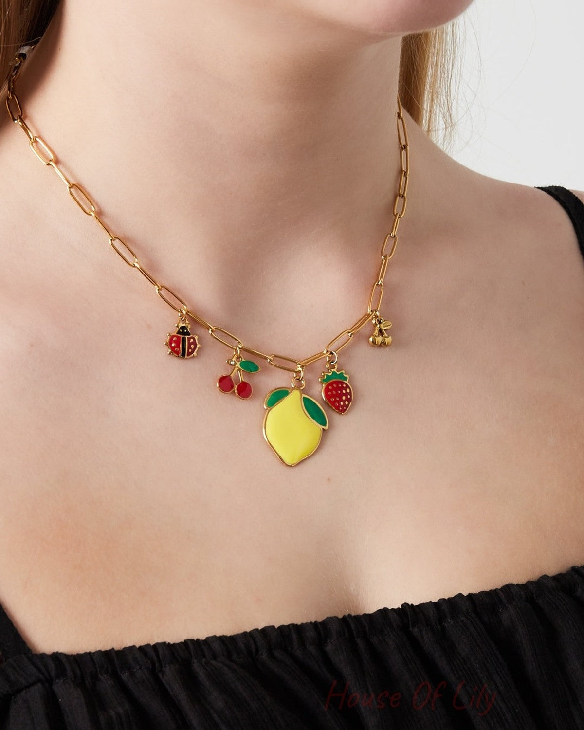 Close-up of a woman wearing the gold-tone paperclip chain necklace with fruit and ladybug charms over a black top
