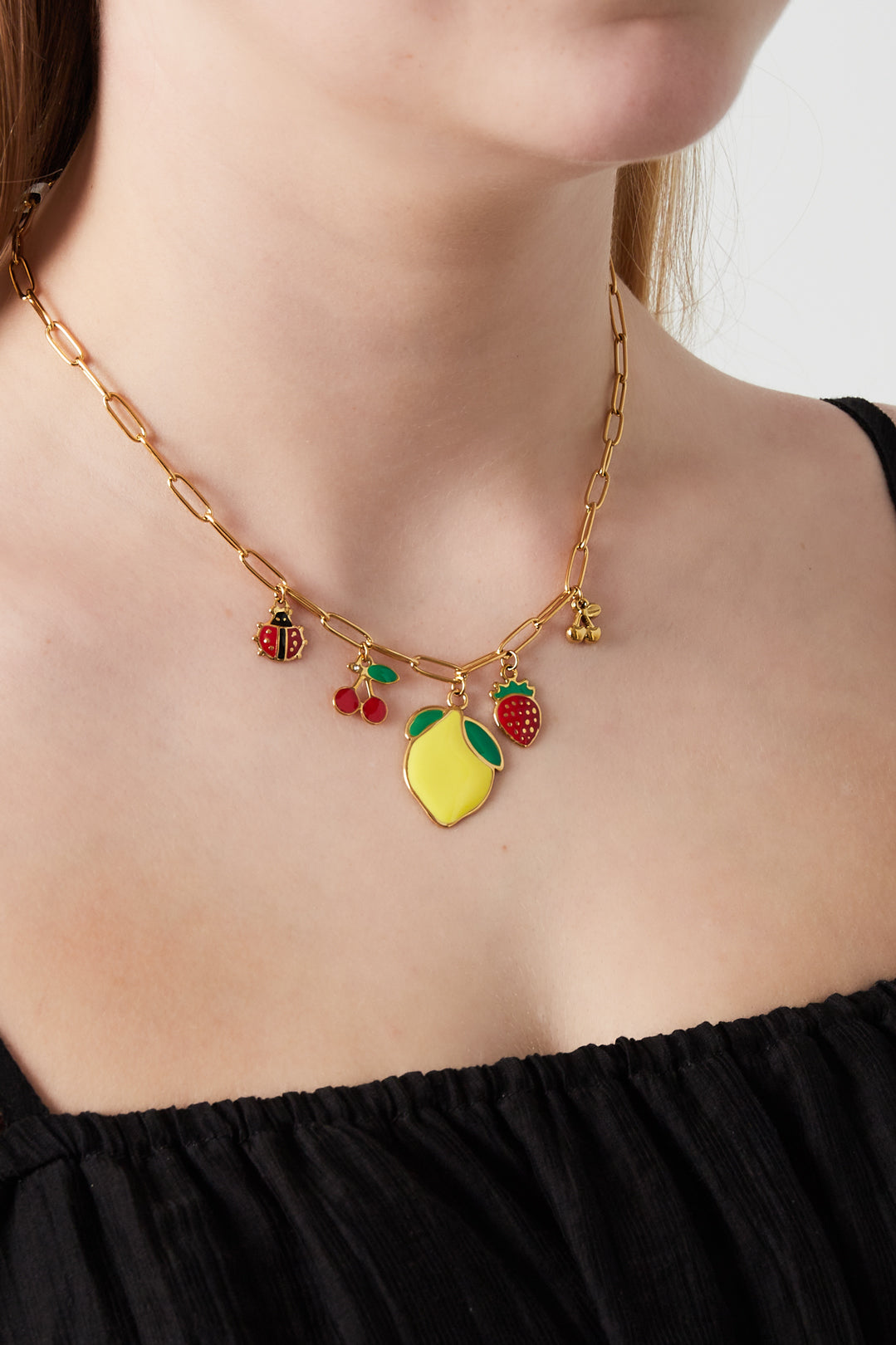 Close-up of a woman wearing the gold-tone paperclip chain necklace with fruit and ladybug charms over a black top