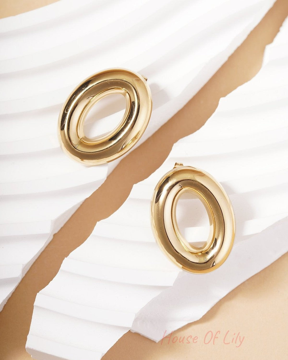 Orbit Chaos Hoops: Shiny gold-tone oval-shaped earrings with a smooth, chunky modern design on white abstract displays.
