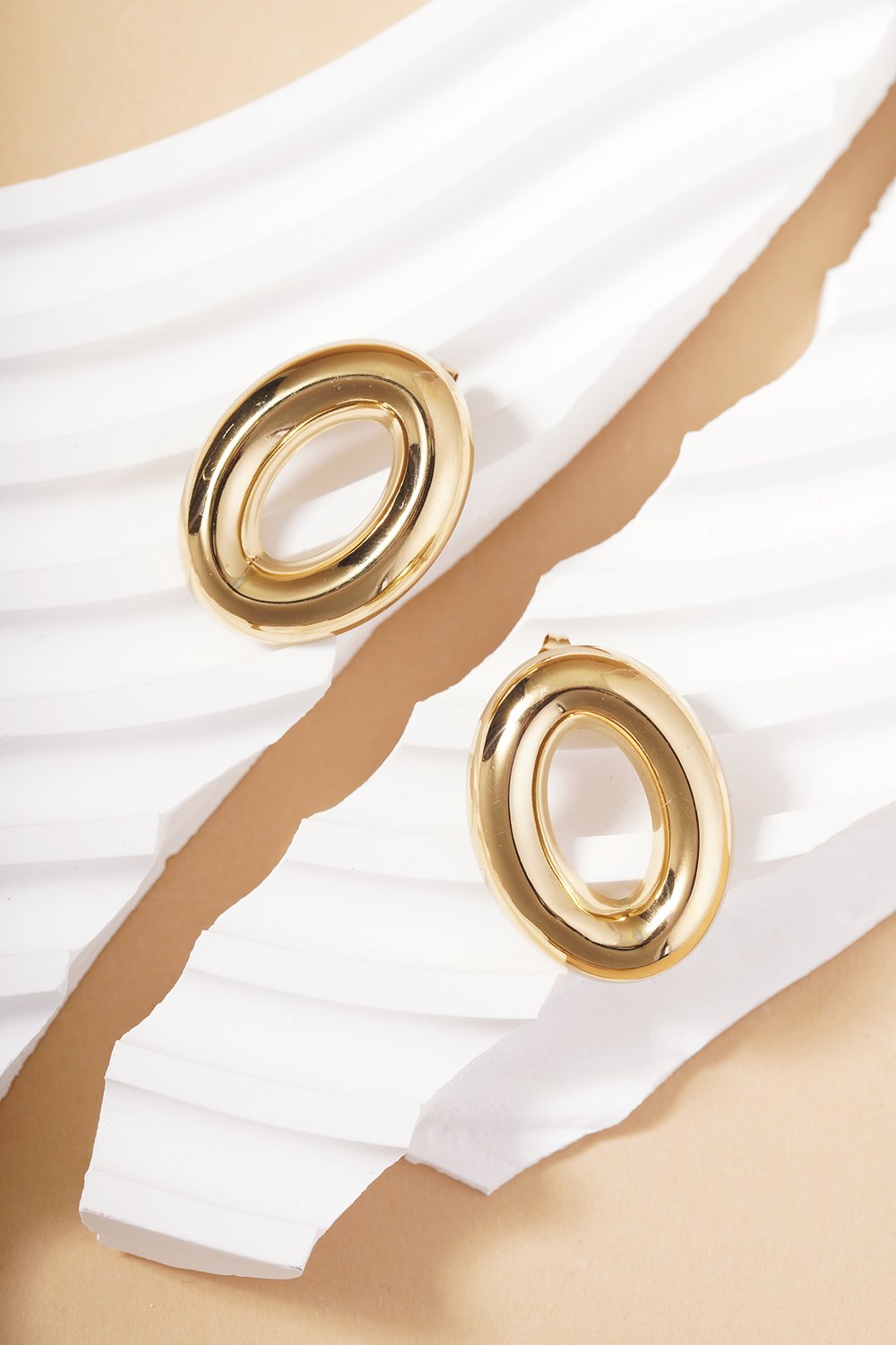Orbit Chaos Hoops: Shiny gold-tone oval-shaped earrings with a smooth, chunky modern design on white abstract displays.