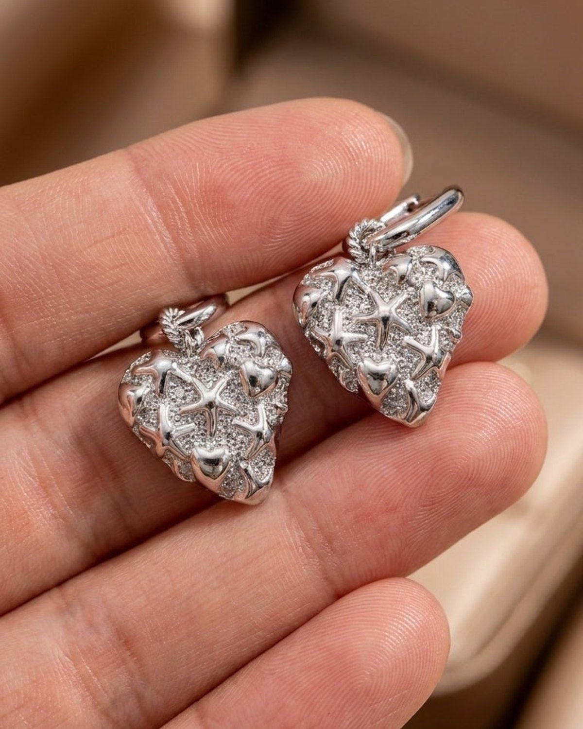 Silver-tone squoval hoop earrings with puffed heart charms featuring raised starfish, mini hearts, and textured pave details.