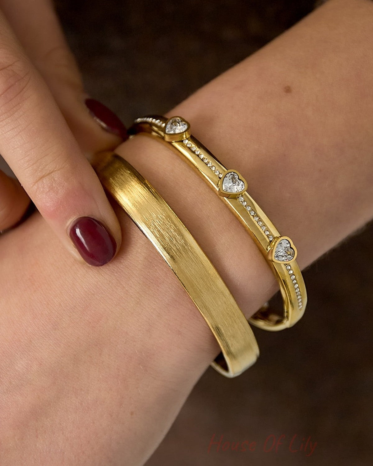 Close-up of wrist wearing gold brushed metal cuff bracelet paired with a delicate heart charm bracelet