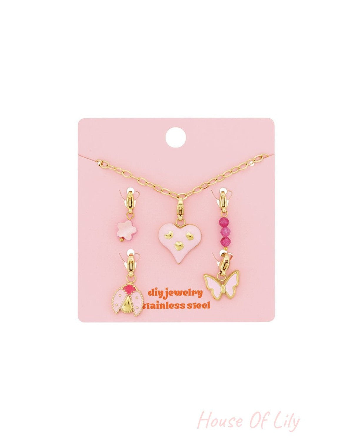 Gold chain charm bracelet set with pink enamel heart, ladybug, butterfly, flower, and beaded charms on a pink card.