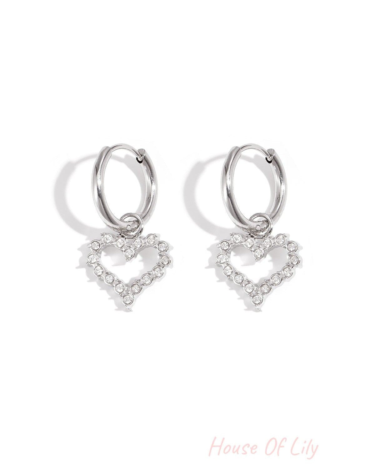 Silver-tone hoop earrings with dangling heart-shaped rhinestone charms on white background