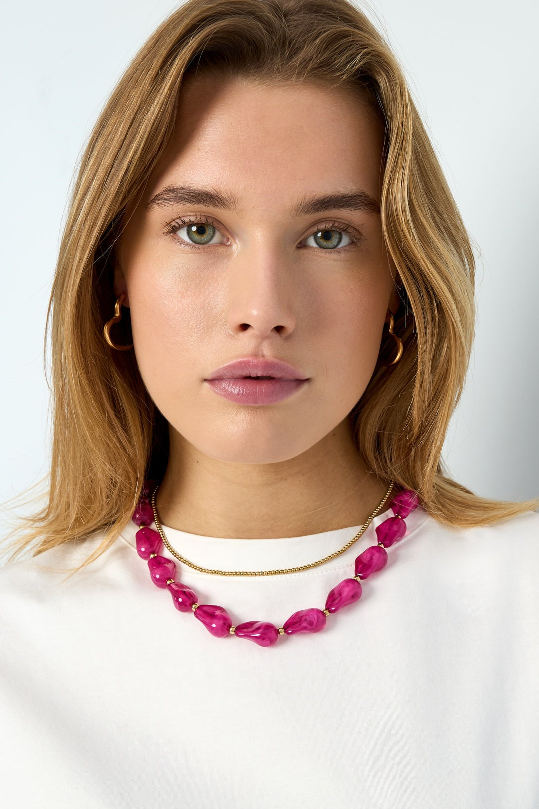 Close-up of woman wearing vibrant pink acrylic chunky beaded necklace with gold-tone chain on white shirt