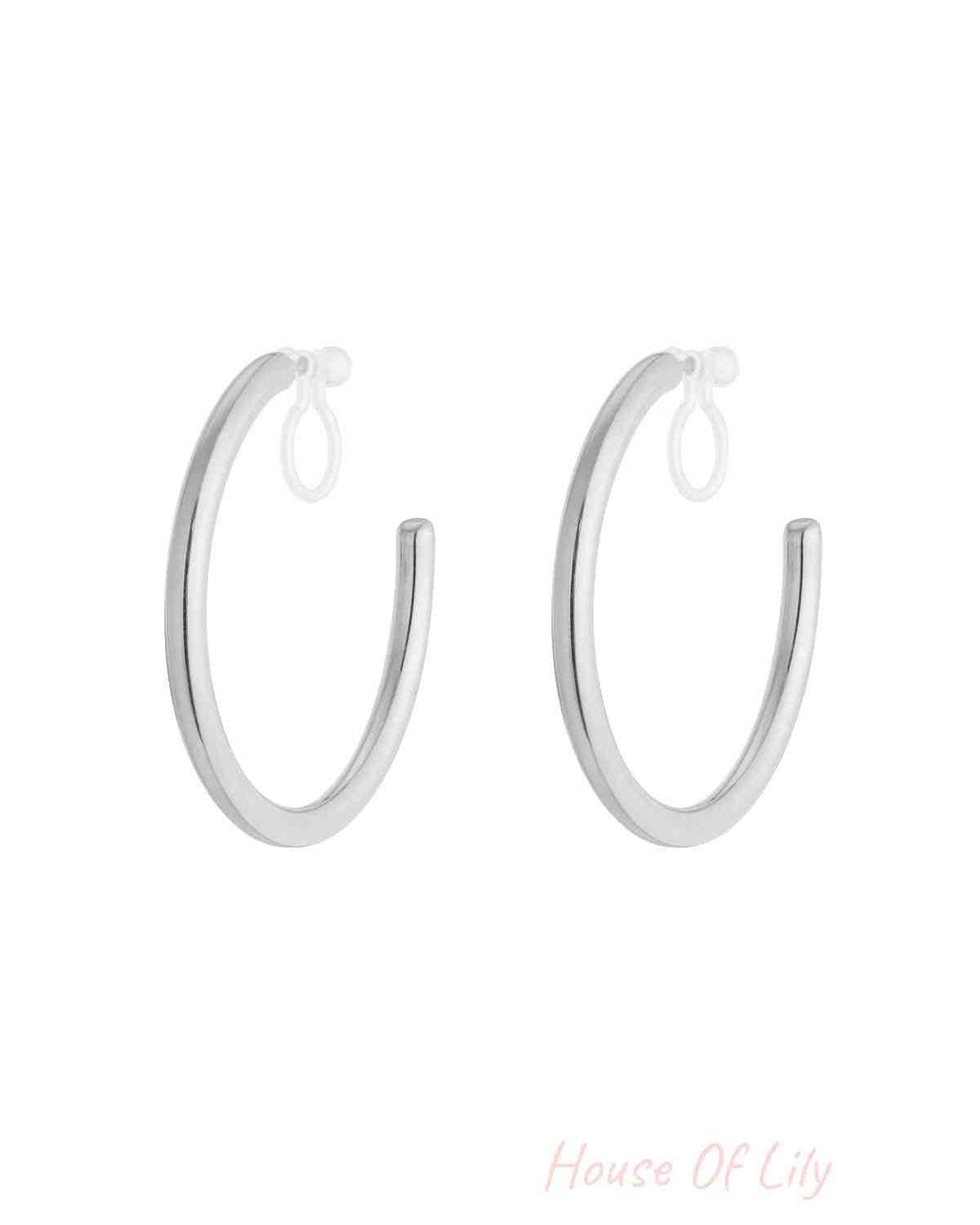 Pair of polished silver-tone clip-on hoop earrings with clear silicone loops on white background