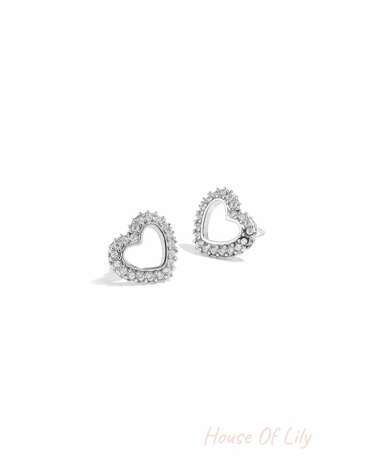 Close-up of silver-tone heart-shaped stud earrings with rhinestone accents on white background