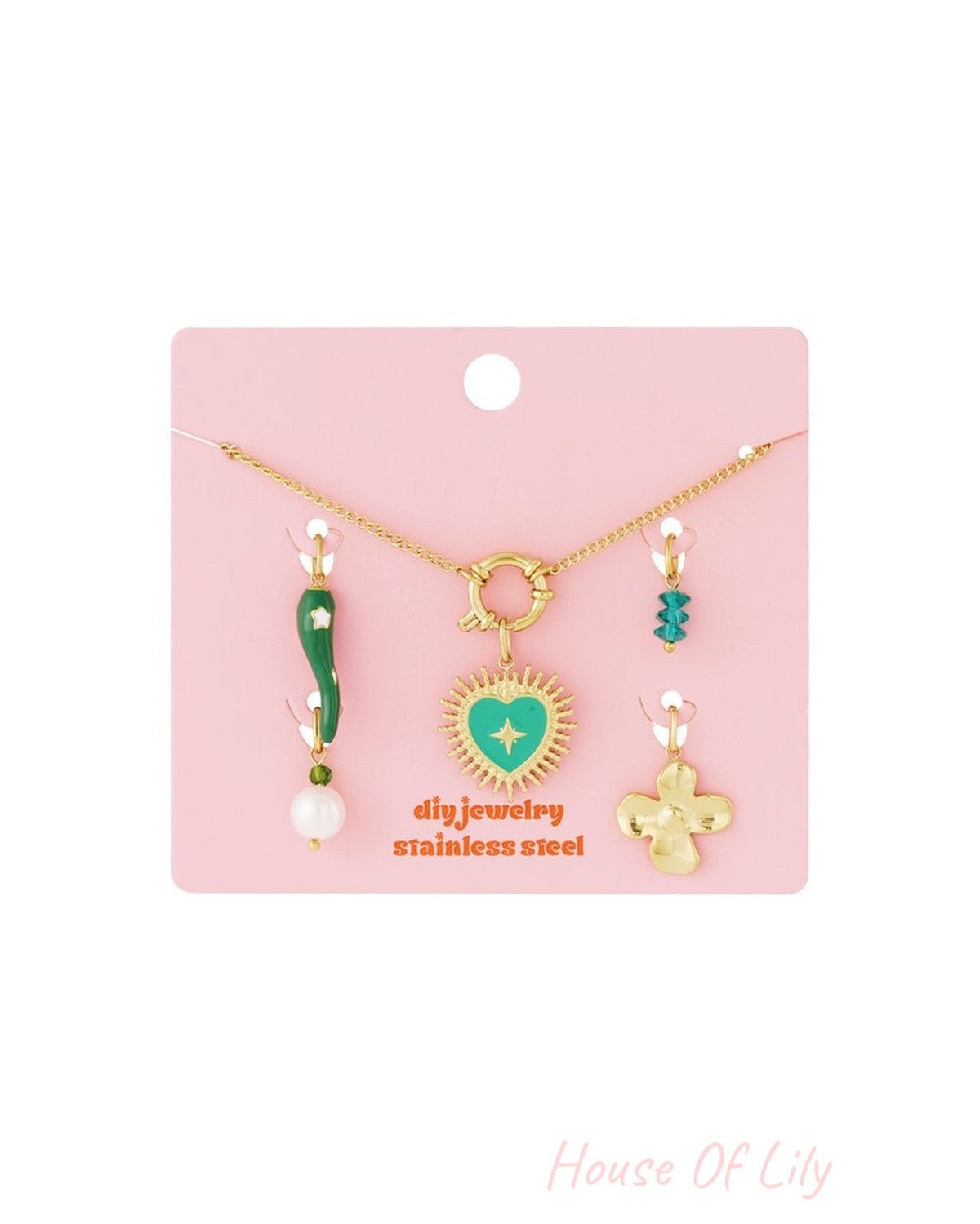 Gold stainless steel necklace with a green enamel heart charm and assorted decorative charms on a pink display card.