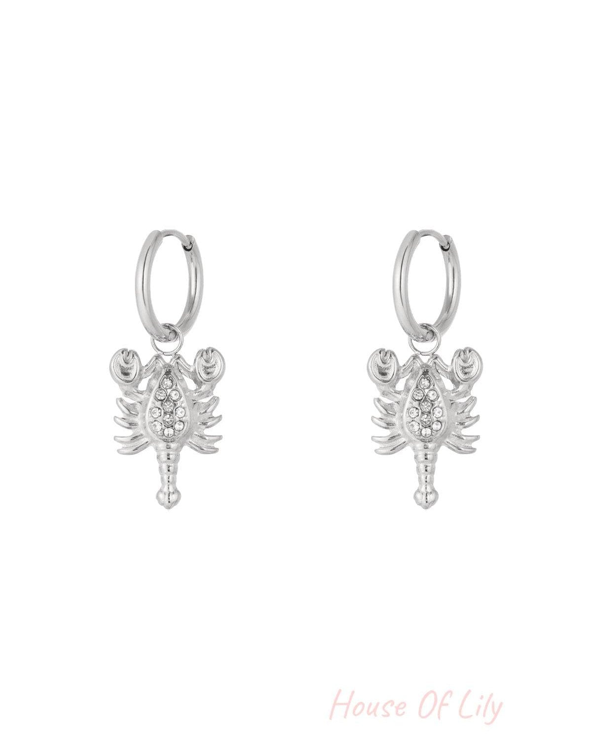 Pair of silver Scorpio charm hoop earrings with rhinestone details on a white background