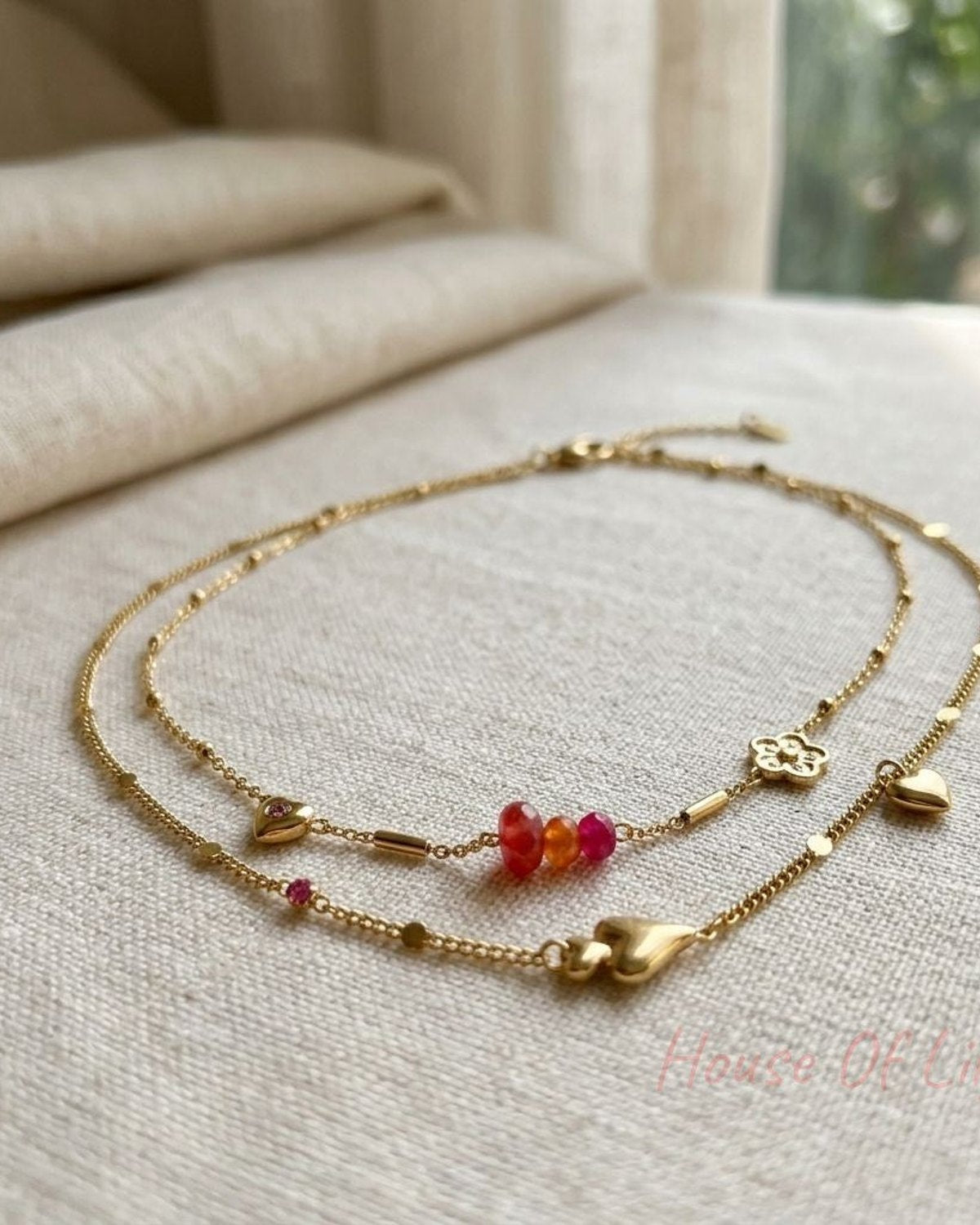 Close-up of the Bloom Heart Duo necklace with flower and heart charms on neutral fabric, highlighting metal and rhinestone details.