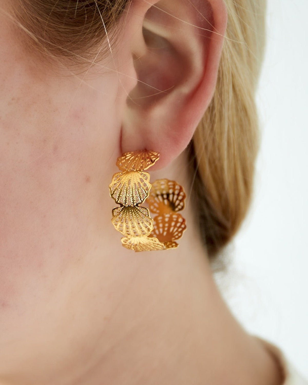 Close-up of a woman wearing gold seashell hoop earrings showcasing their size and intricate design