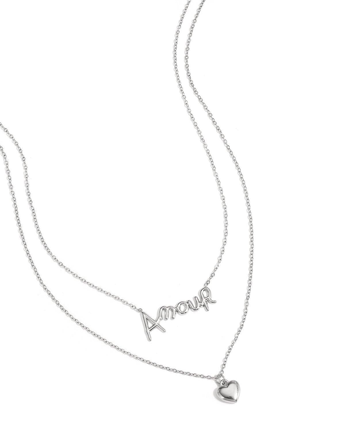 Close-up of silver layered necklace with ‘Amour’ script and heart pendant on white background