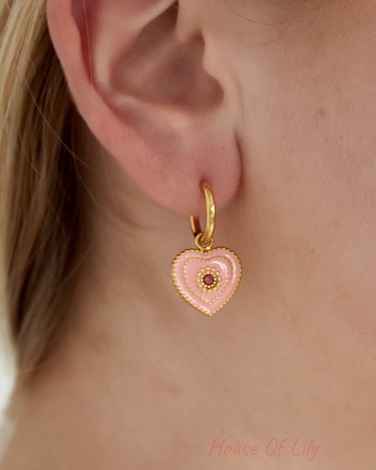 Close-up of ear wearing a gold-tone hoop earring with a soft pink heart-shaped enamel charm and beaded detailing