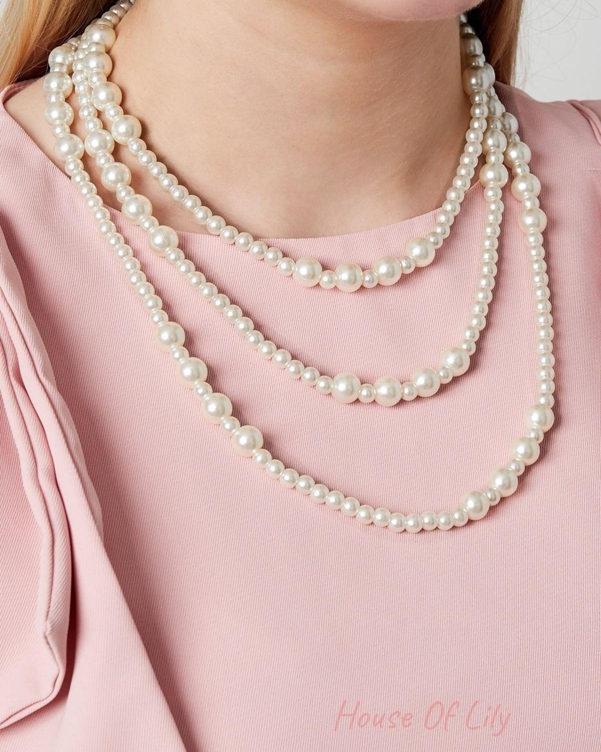Model wearing a three-layered pearl necklace over a sleeveless pink top showing the necklaceβs elegant and youthful style