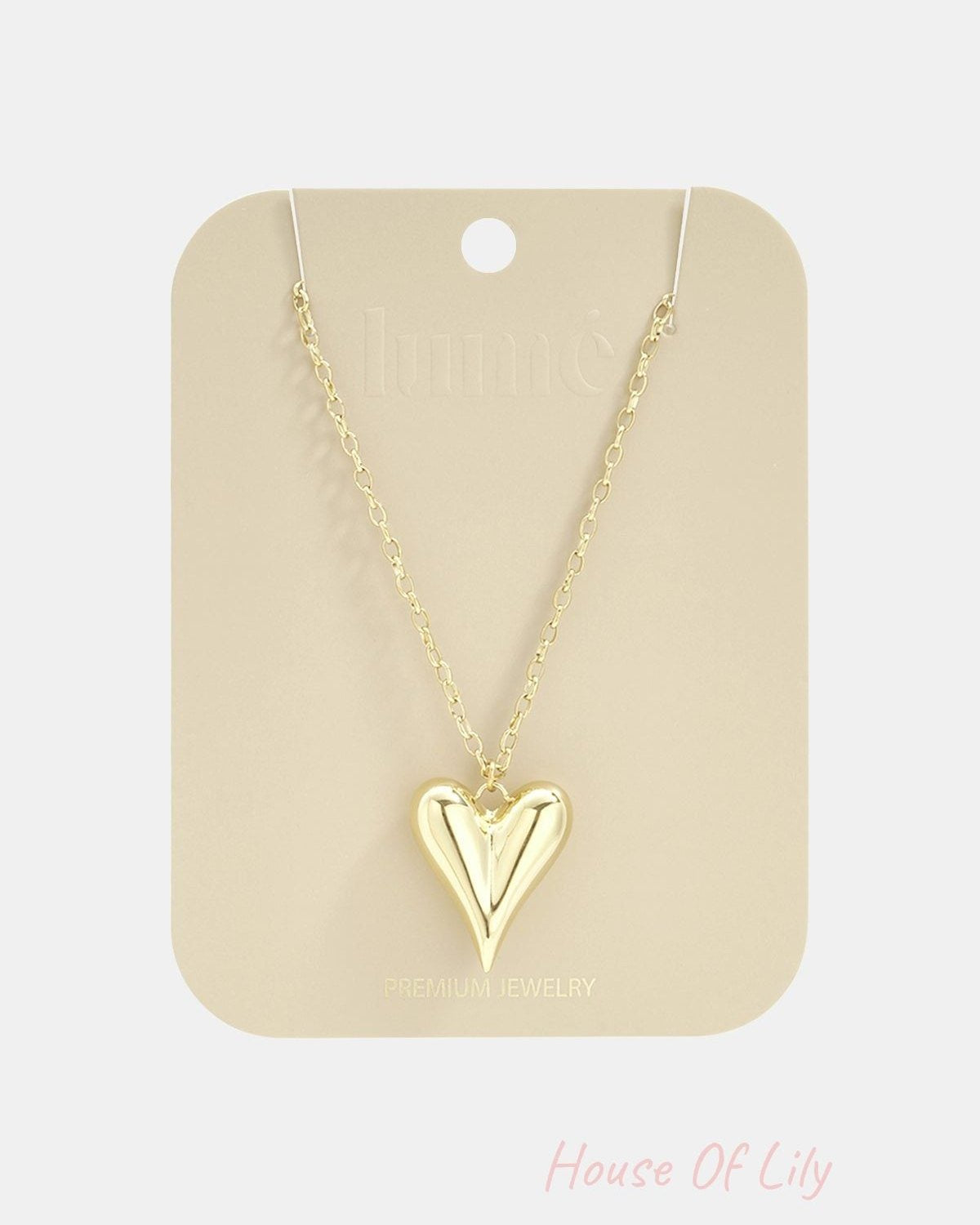 Gold-toned long necklace featuring a smooth, puffed heart pendant on a delicate link chain, displayed on a card.