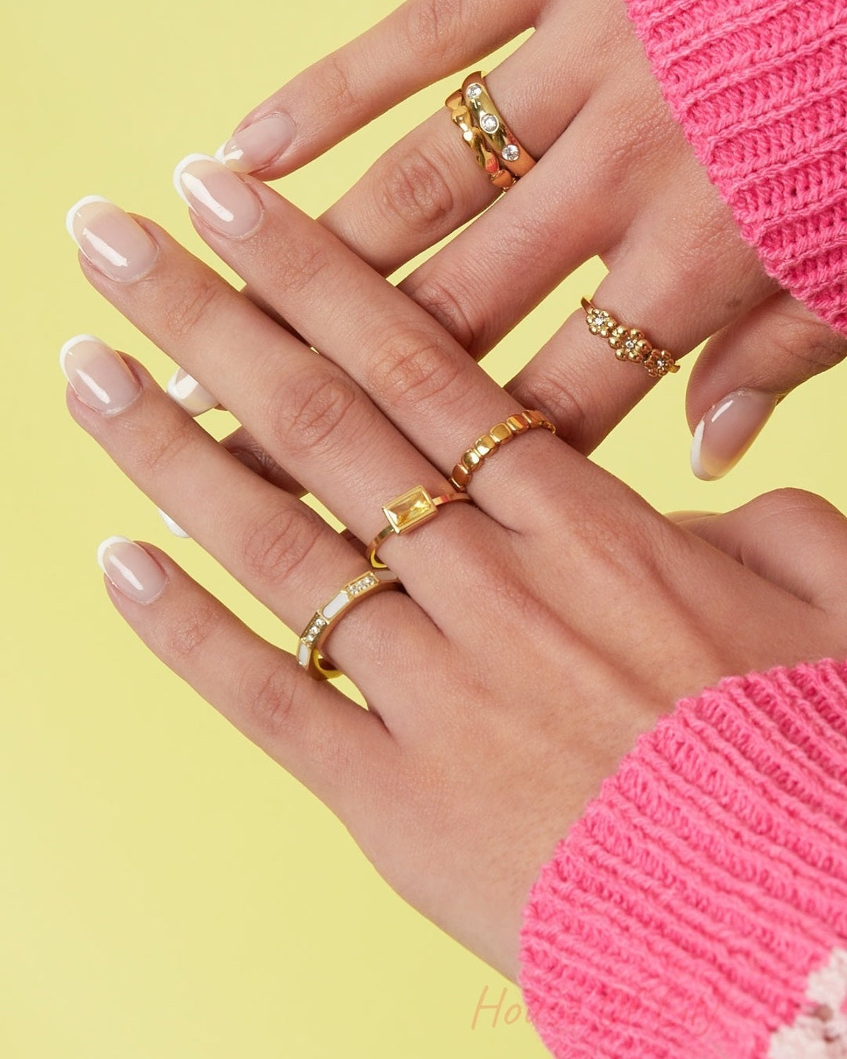 Model hand wearing layered gold rings including geometric gold ring with mother-of-pearl and zircon stones, against a yellow background