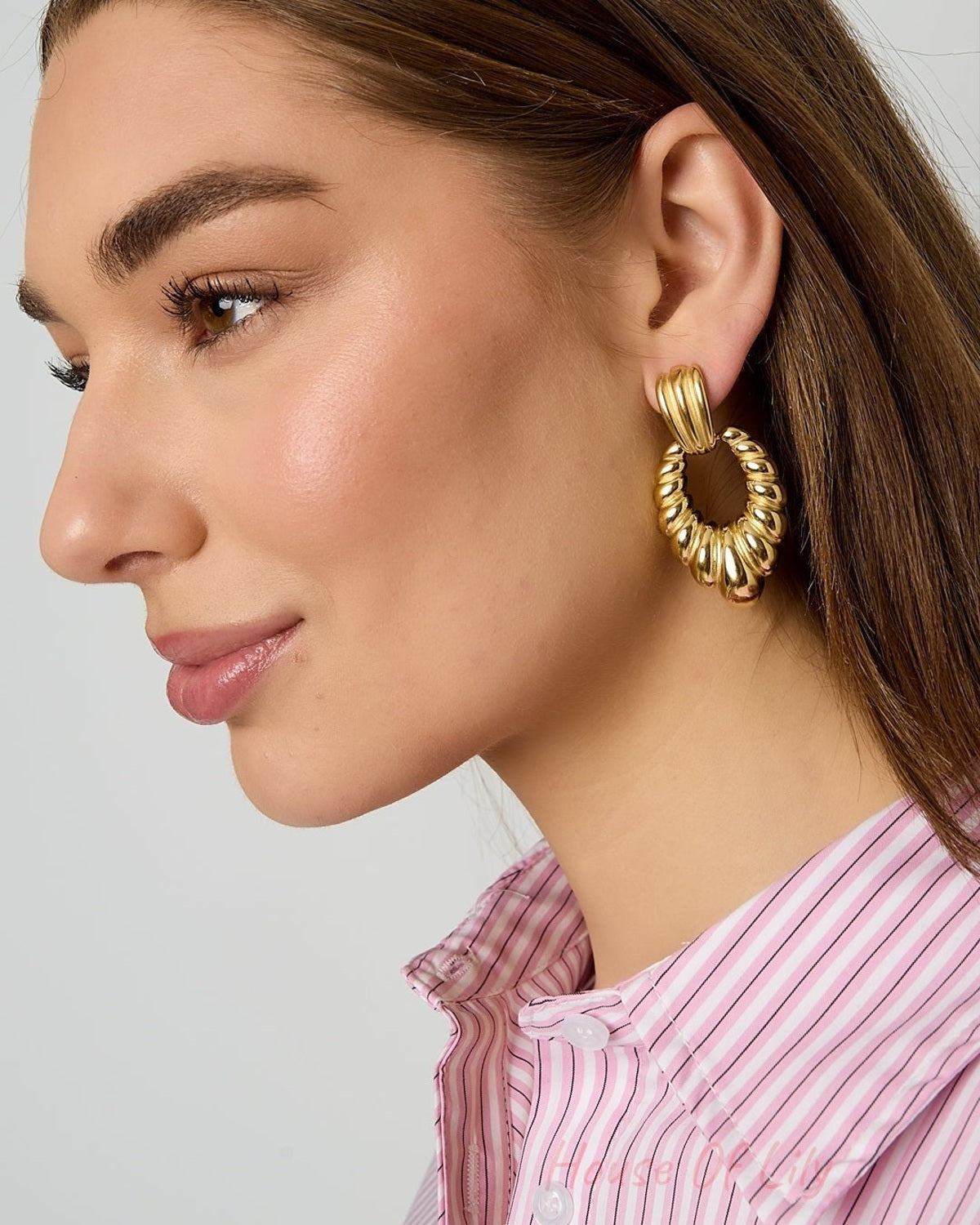 Close-up side profile of model wearing twisted gold hoop earrings showing detailed texture