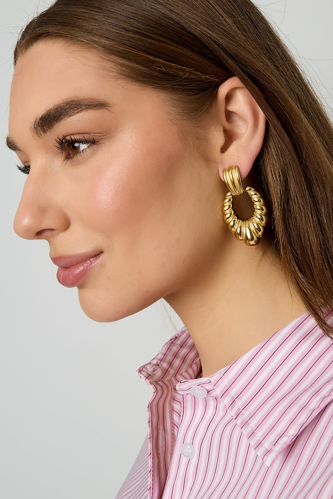 Close-up side profile of model wearing twisted gold hoop earrings showing detailed texture