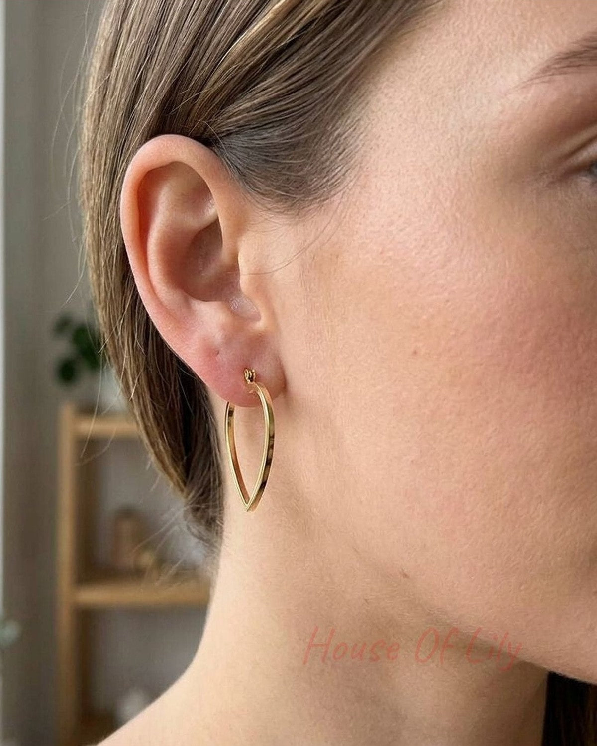Close-up of heart-shaped stainless steel hoops hanging from a model's pierced ears with natural daylight and neutral background.