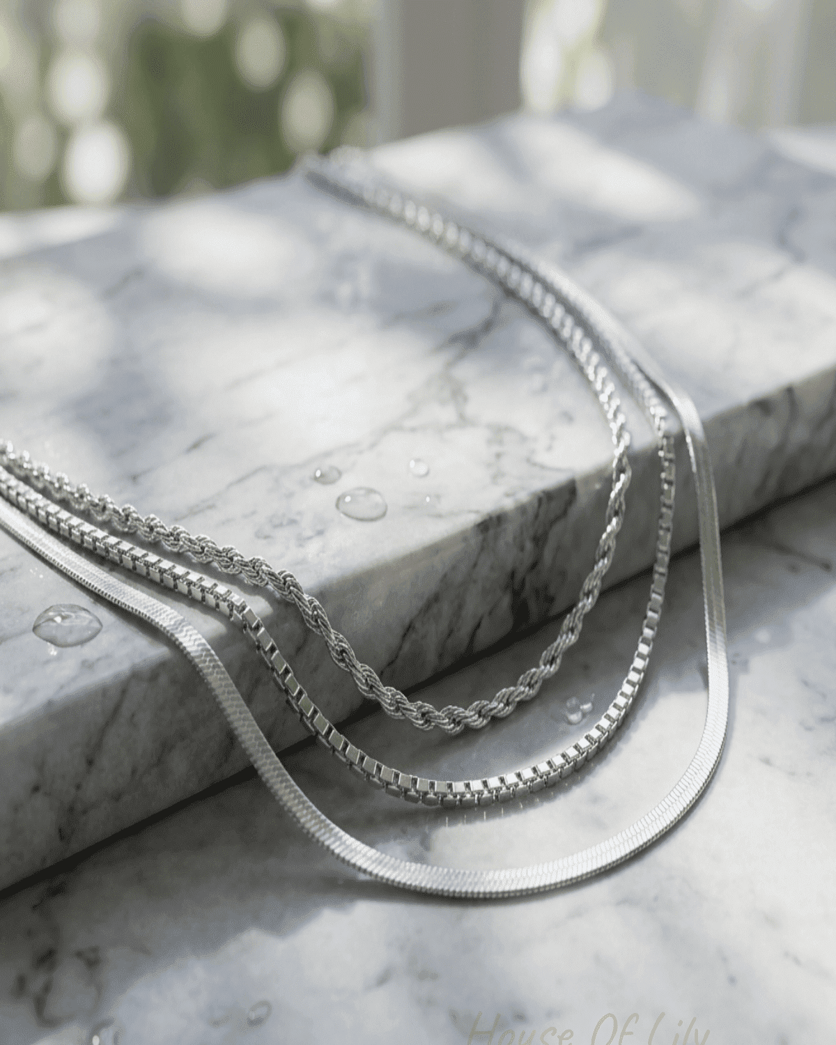 Close-up of a multi-layer gold chain necklace on a reflective textured surface, highlighting intricate micro-texture details and luxurious shine.