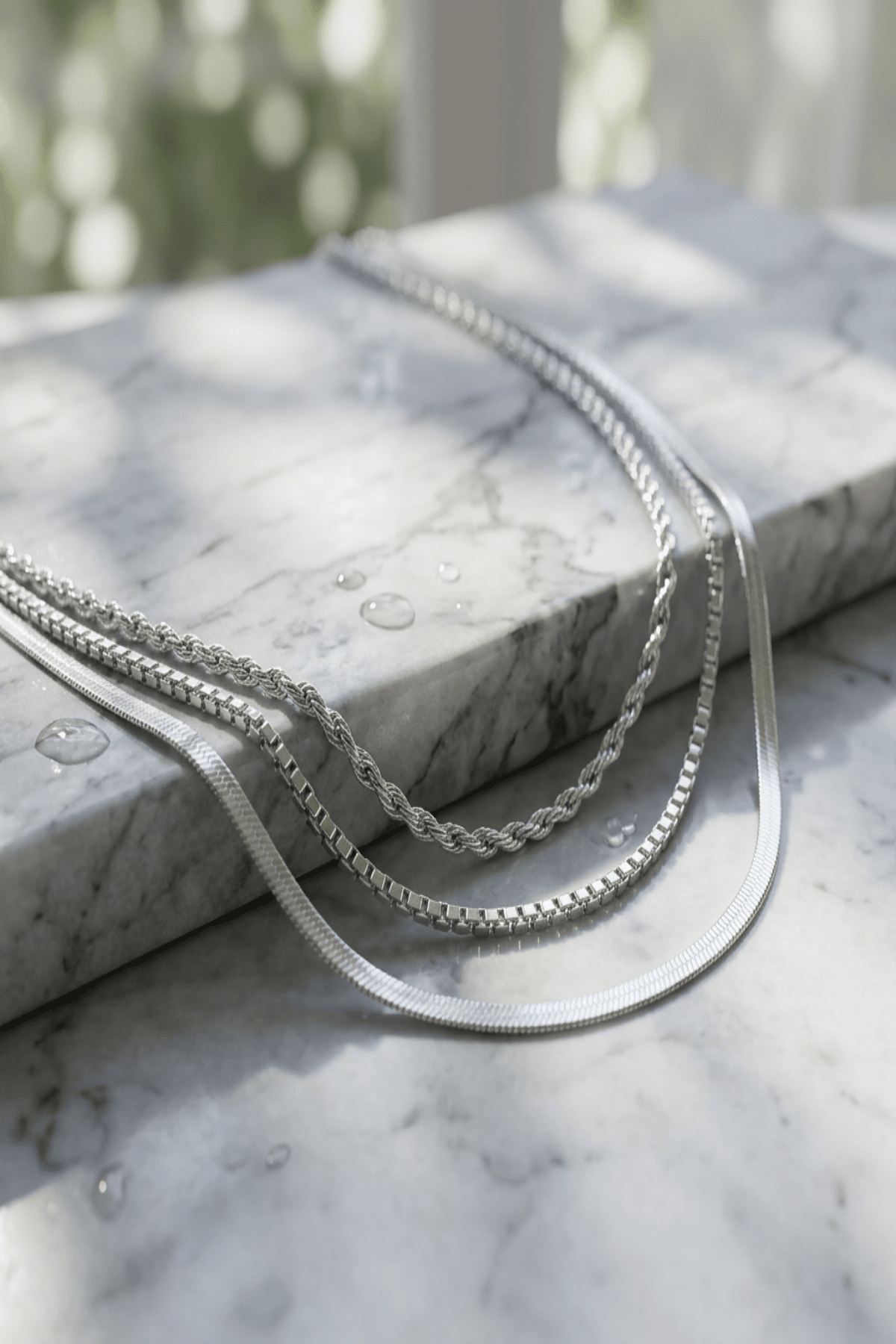 Close-up of a multi-layer gold chain necklace on a reflective textured surface, highlighting intricate micro-texture details and luxurious shine.