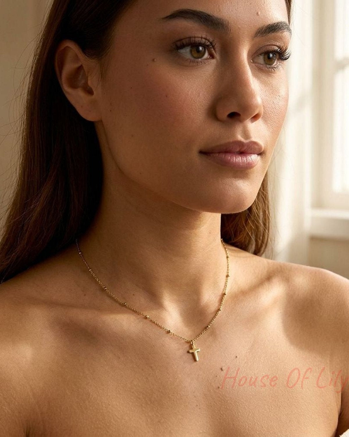 Close-up of stainless steel 'Cross My Heart Chain' with minimalist cross pendant on a model's neck in a softly lit cozy setting.