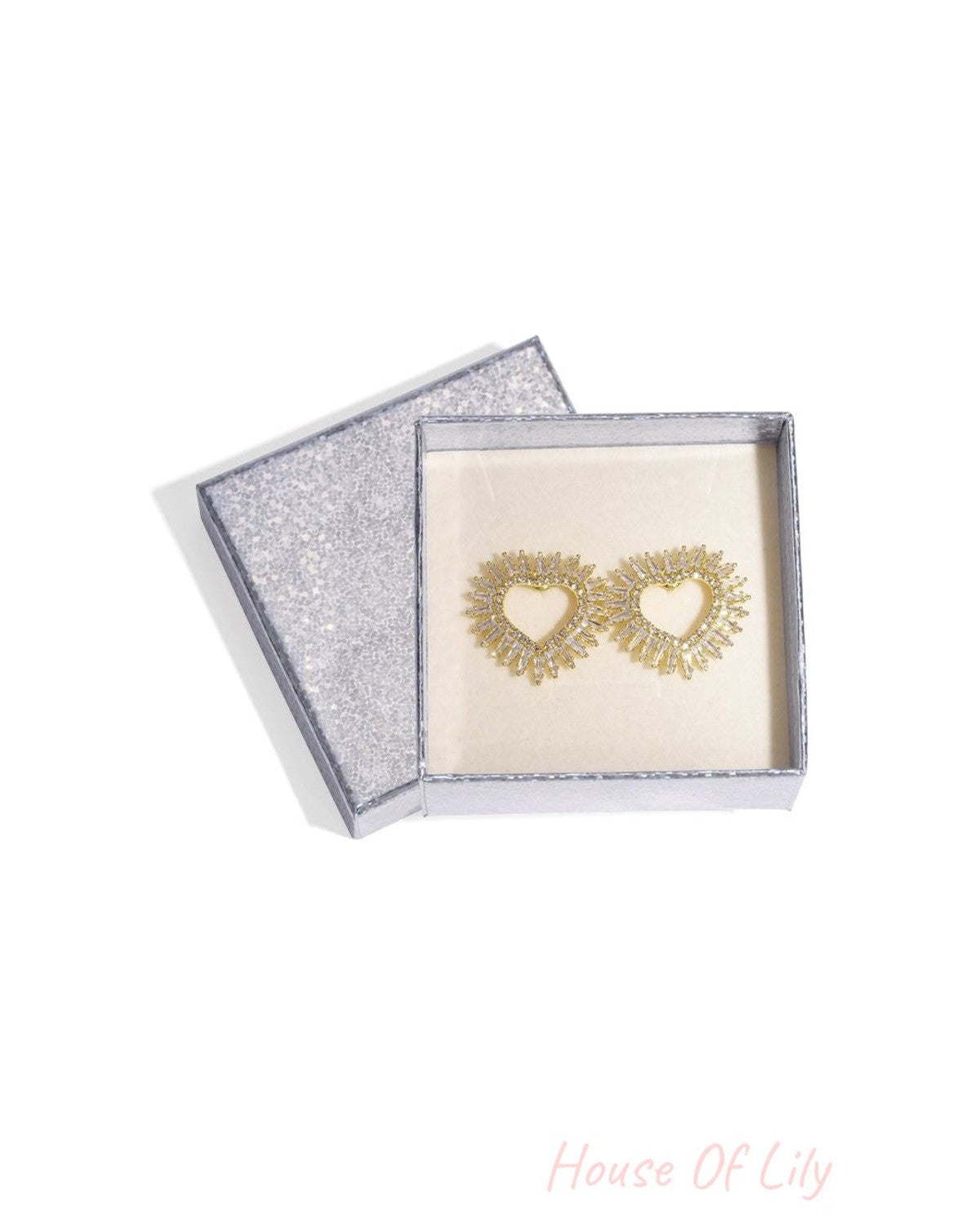 Soft Heart Chaos gold-tone heart-shaped stud earrings featuring sunburst baguette-cut crystals in a glittery gift box.