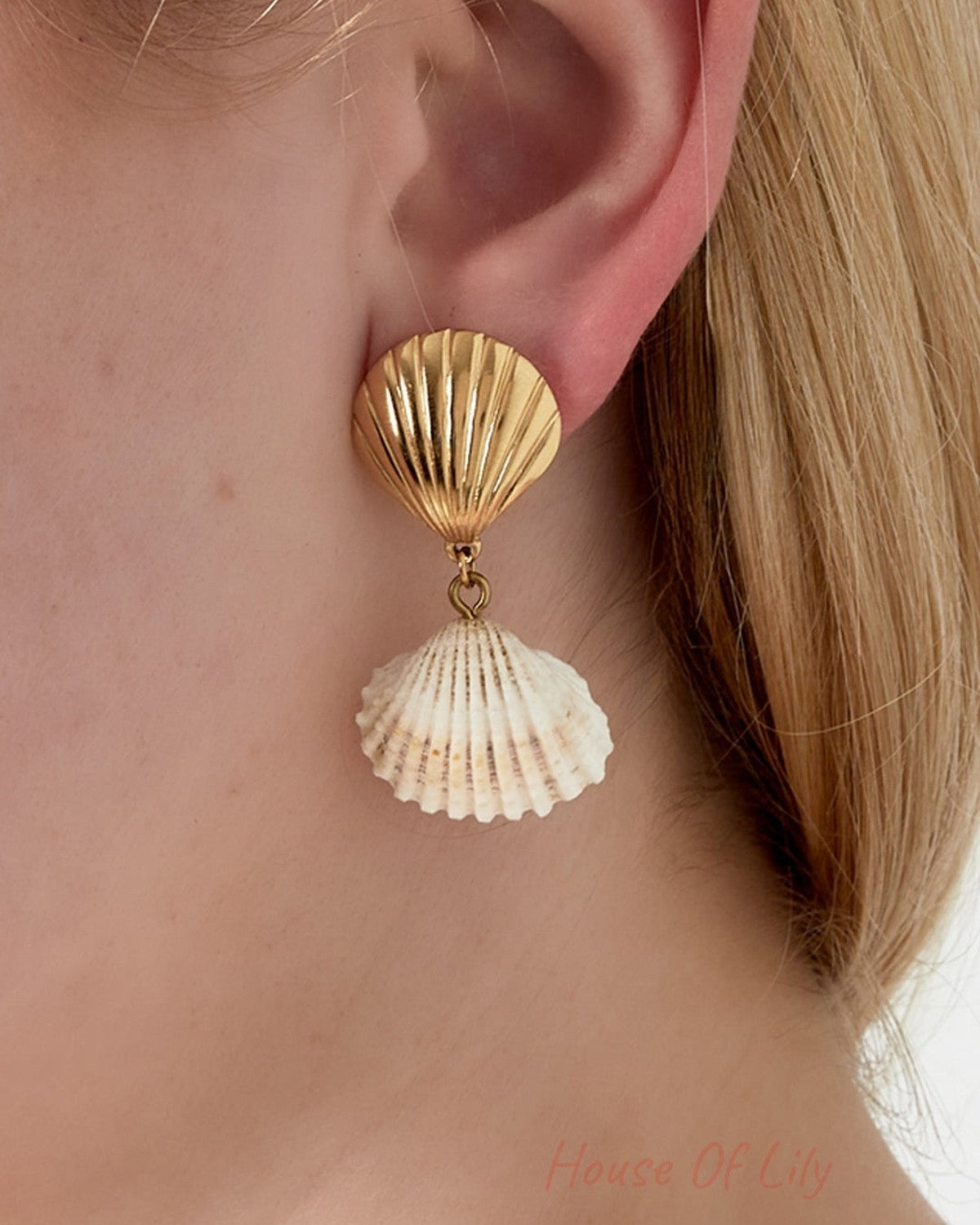 Close-up of a woman wearing a gold-toned seashell drop earring with a natural white seashell pendant