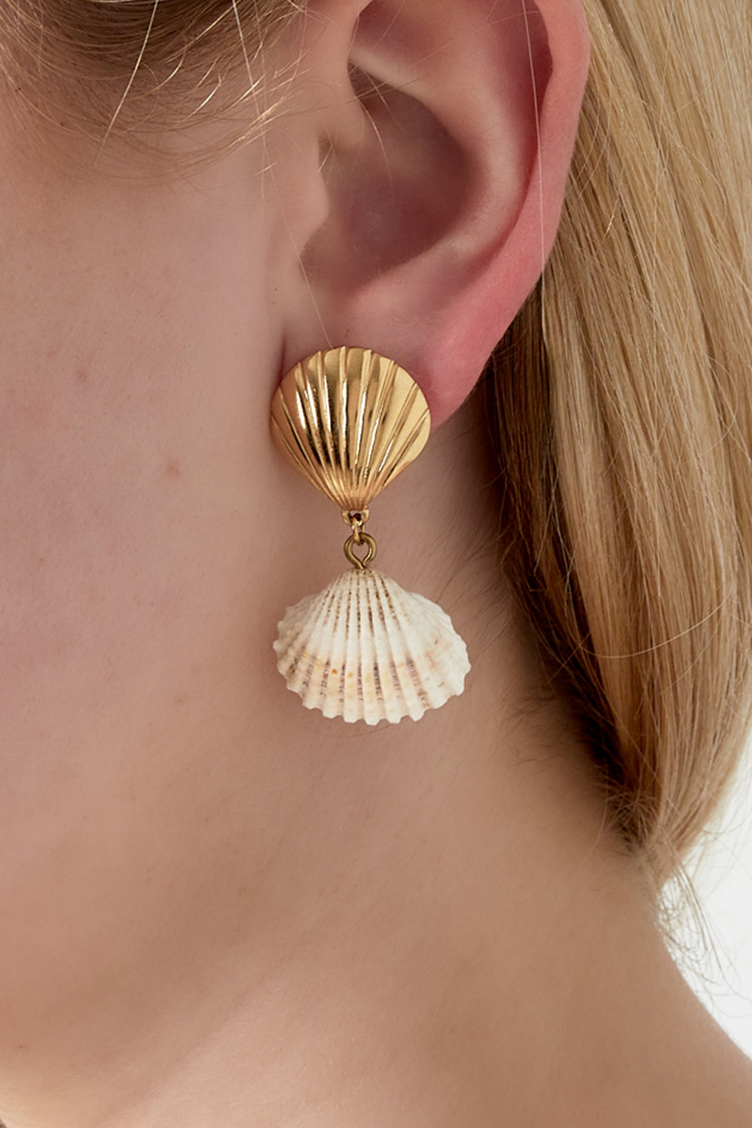 Close-up of a woman wearing a gold-toned seashell drop earring with a natural white seashell pendant