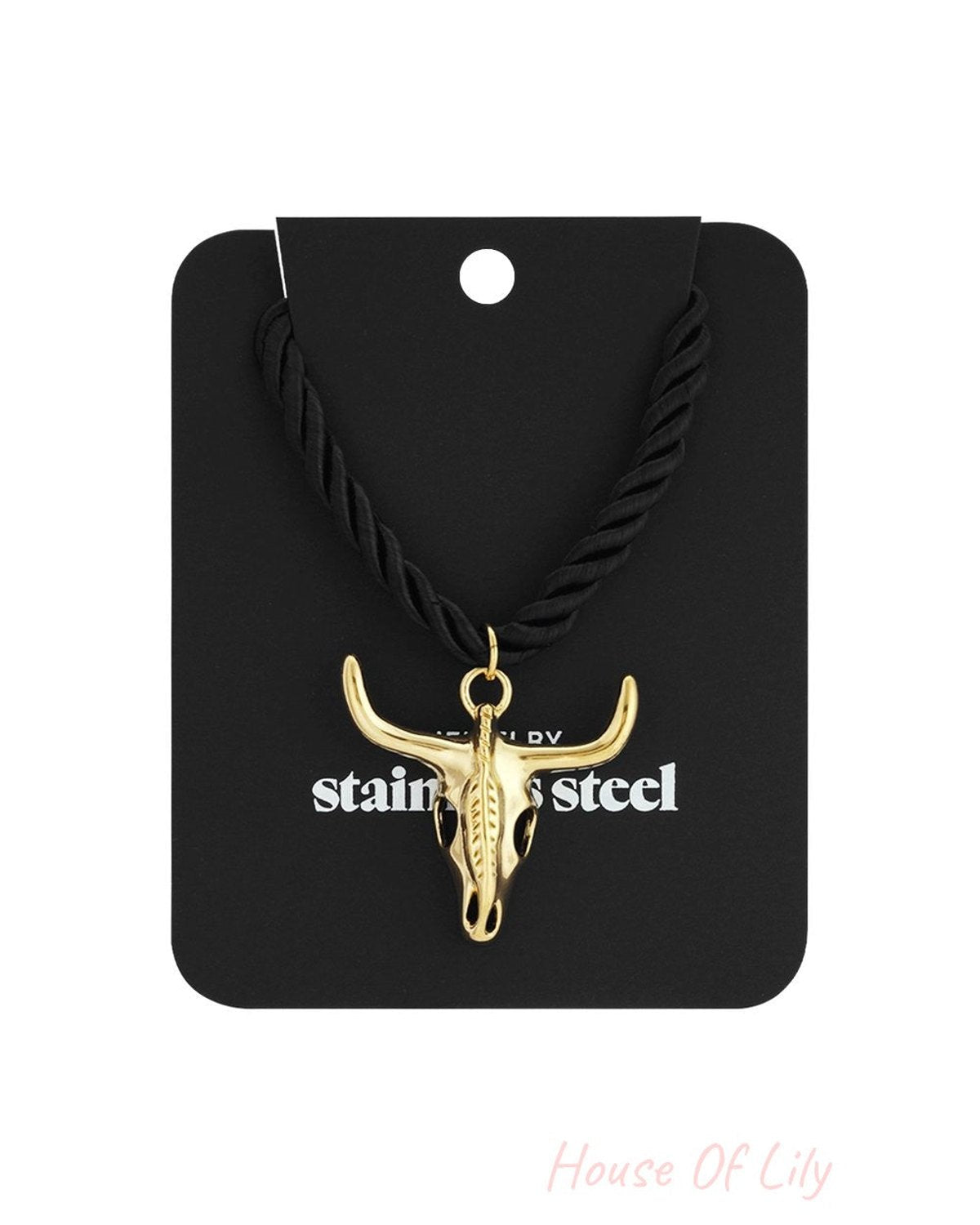 Gold-tone stainless steel bull skull pendant on a black twisted rope necklace against a black display card.