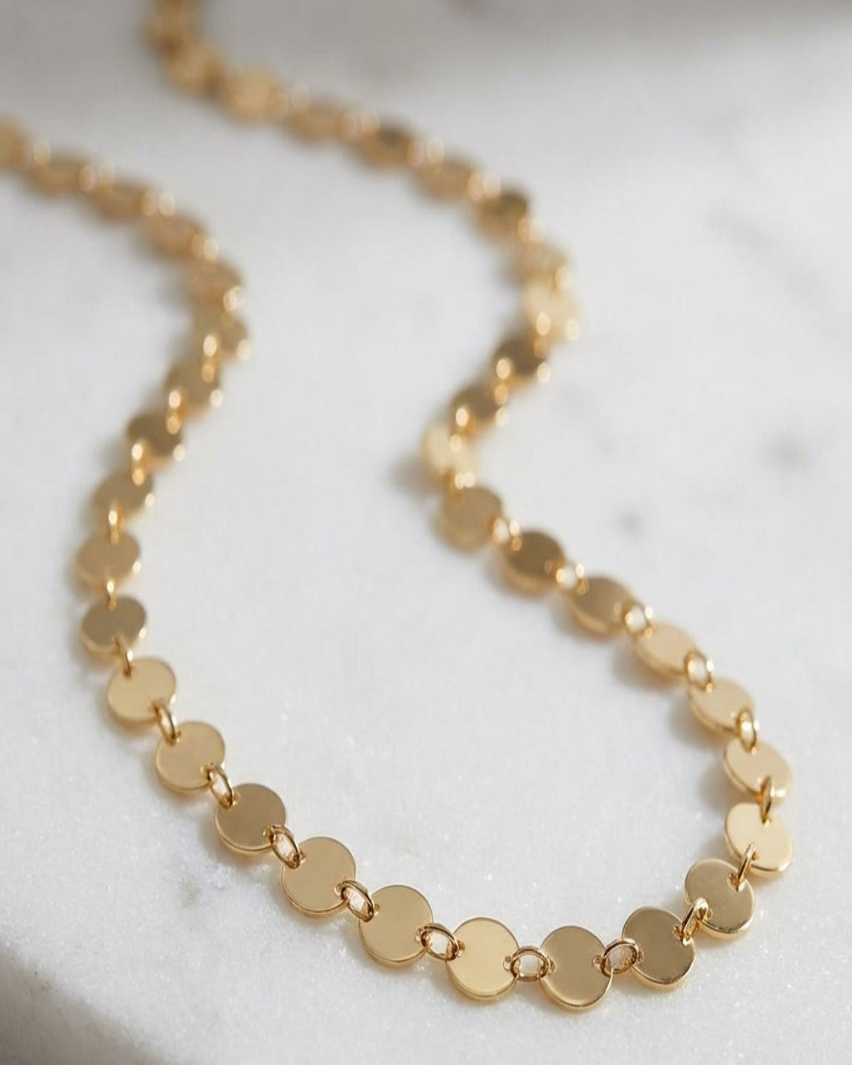 Close-up of Dainty Disc Chain Necklace with reflective discs on textured white marble, showcasing fine links and polished stainless steel finish.