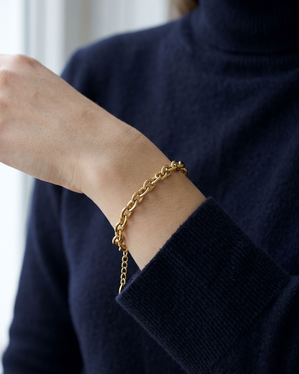 A minimalist polished stainless steel chain bracelet worn on a wrist over a dark navy turtleneck sweater.