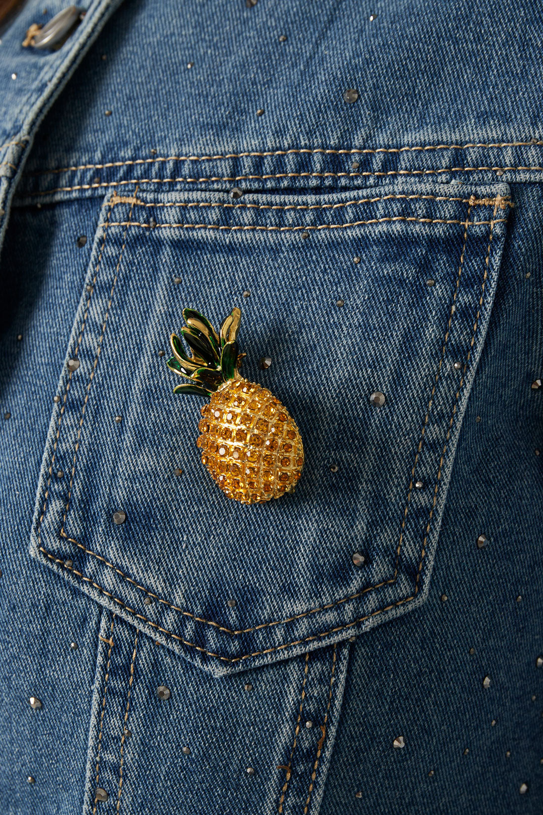 Sparkling pineapple brooch pinned on blue denim jacket pocket decorated with small rhinestones