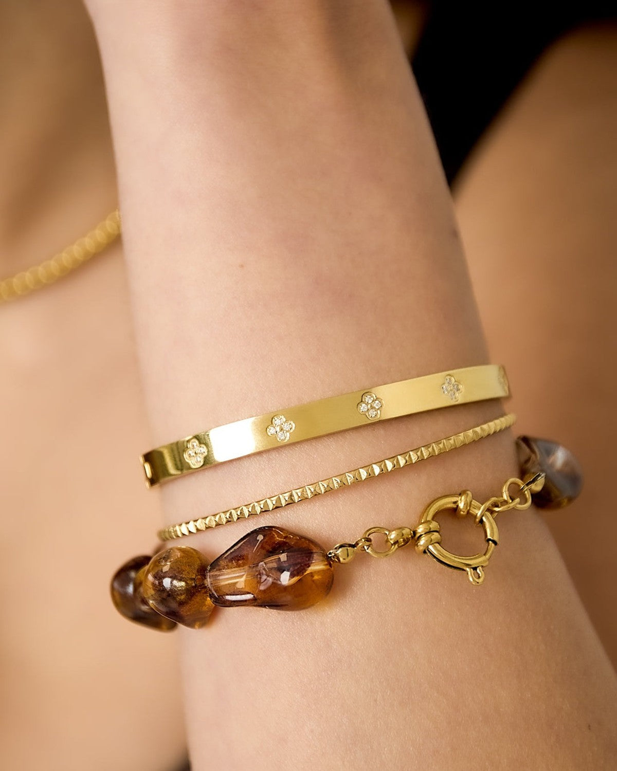 Close-up of a woman's wrist wearing an amber acrylic beaded bracelet stacked with gold bracelets