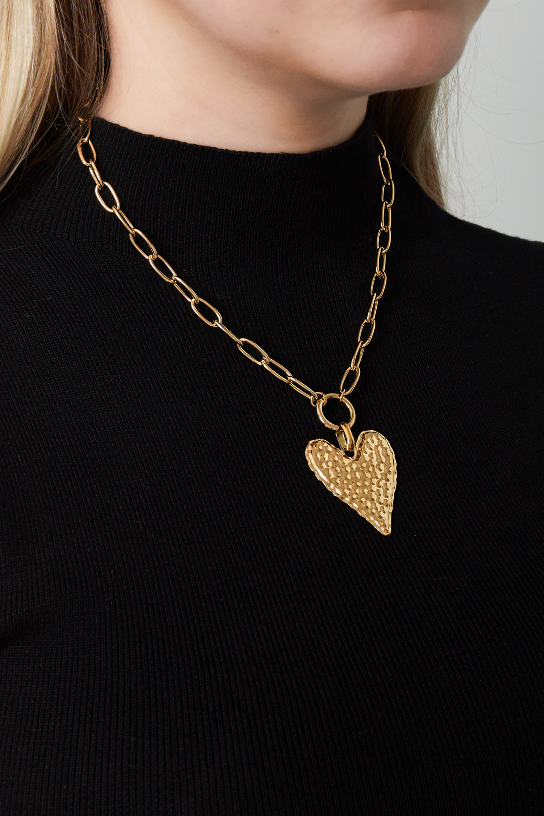 Woman wearing a gold-plated hammered heart pendant necklace paired with a black top
