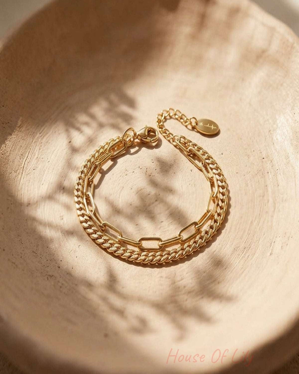 Close-up of a small, double-layered stainless steel bracelet on a textured clay background, highlighting its irregular shape and reflective surface.