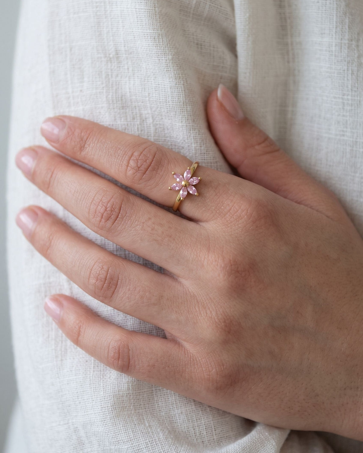 Close-up of a petite floral crystal ring worn on a woman's finger against a neutral linen background.