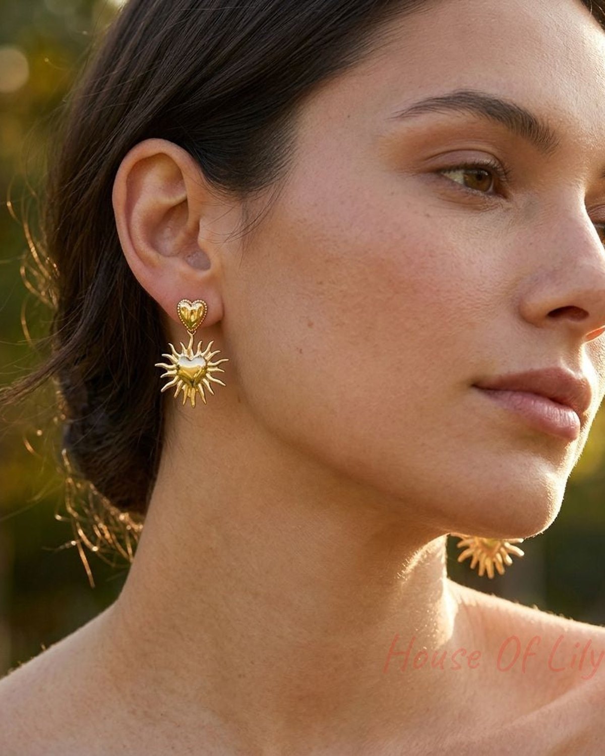 Small 'Golden Sun Heart Dangles' earrings on a model in a sunny outdoor setting, catching light and highlighting their delicate design.