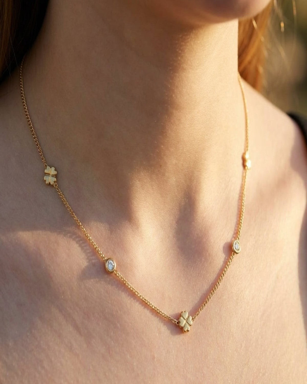 High-resolution close-up of a petite gold Lucky Clover Chain Necklace worn on a female model's collarbone, featuring tiny clover charms and sparkling rhinestones in warm golden hour lighting.
