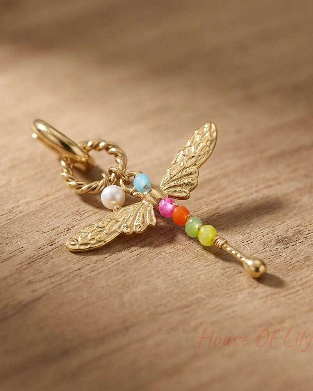 Small stainless steel dragonfly earrings with butterfly back, resting on textured wood surface, showcasing fine details and shape.