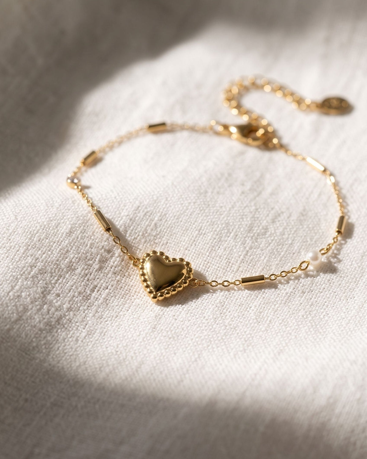 Dainty stainless steel heart charm bracelet with zircon resting on textured white linen fabric.