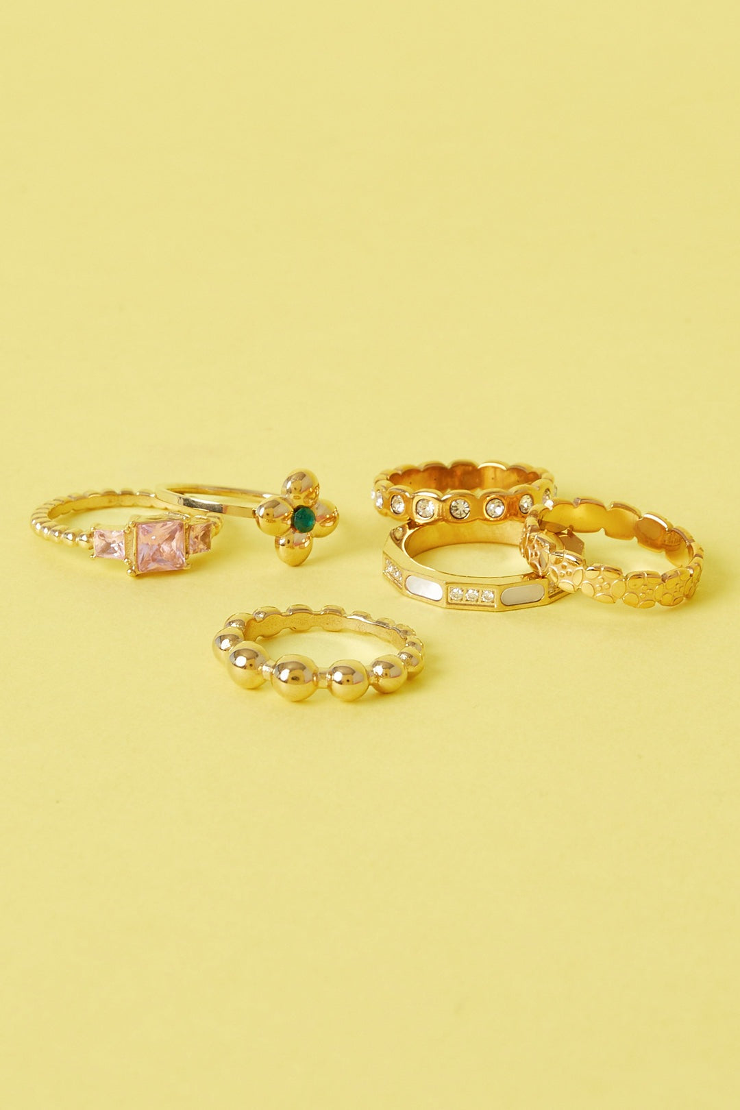 Collection of six gold rings with varied designs including gemstone accents and textured bands on a yellow background