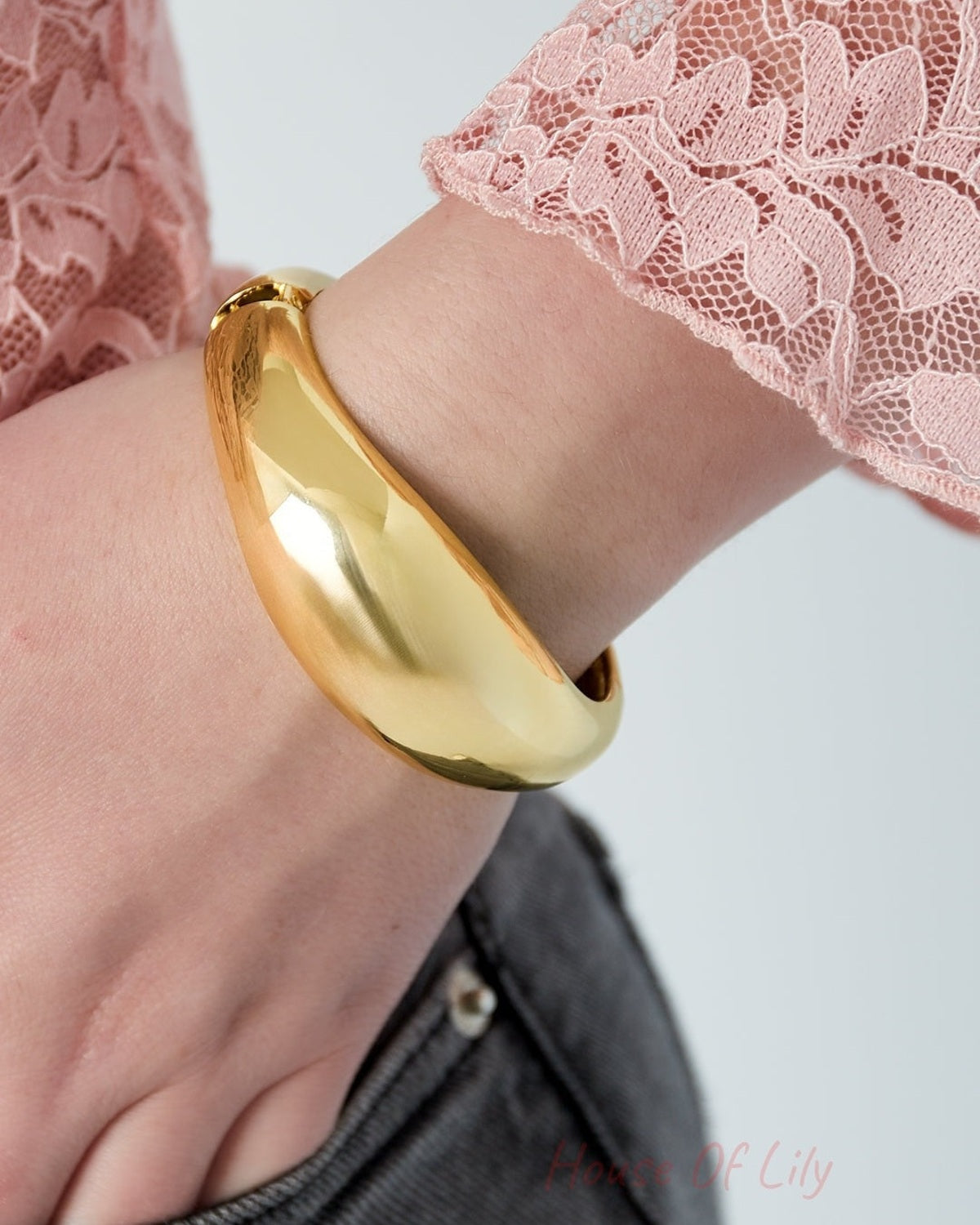 Close-up of gold dome-shaped bangle bracelet worn on wrist with pink lace sleeve and denim