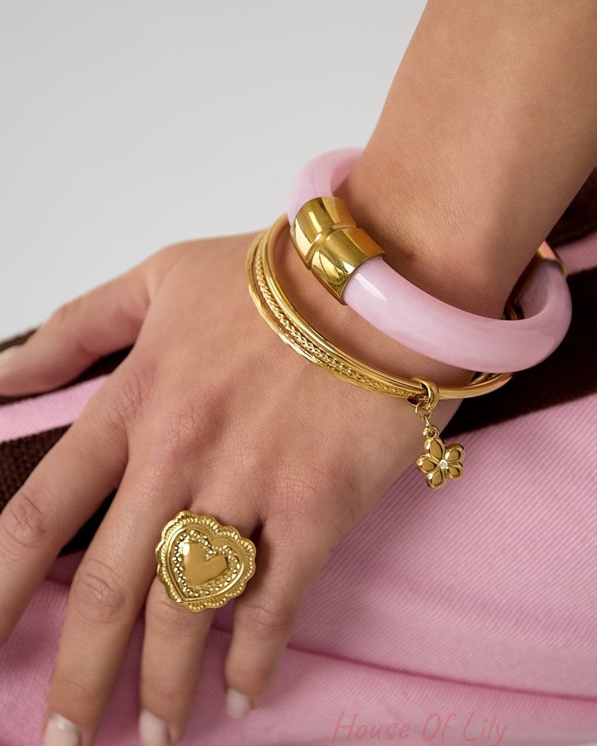 Woman's wrist wearing gold bangles with flower charm alongside pink bangle and gold heart ring