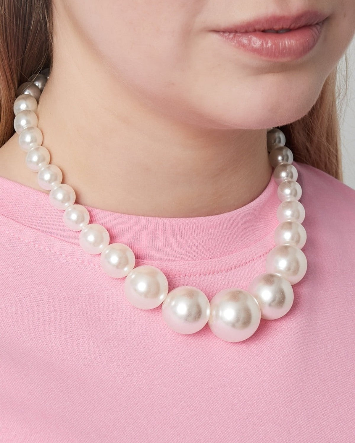 Woman wearing a graduated pearl beaded necklace paired with a pink top, highlighting the necklace's soft and elegant look