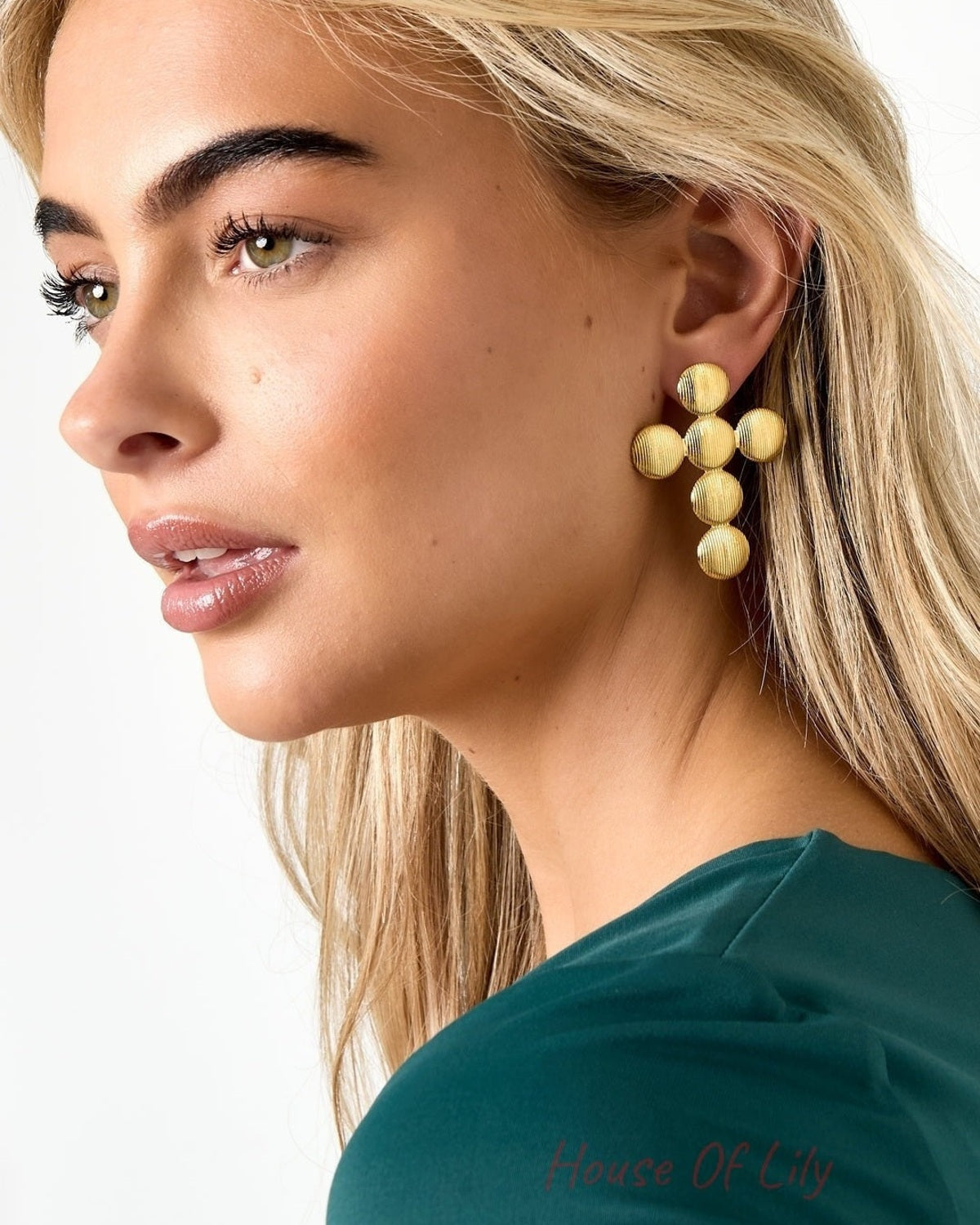 Close-up side profile of a woman wearing large textured gold cross stud earrings with ribbed surface accentuating the design