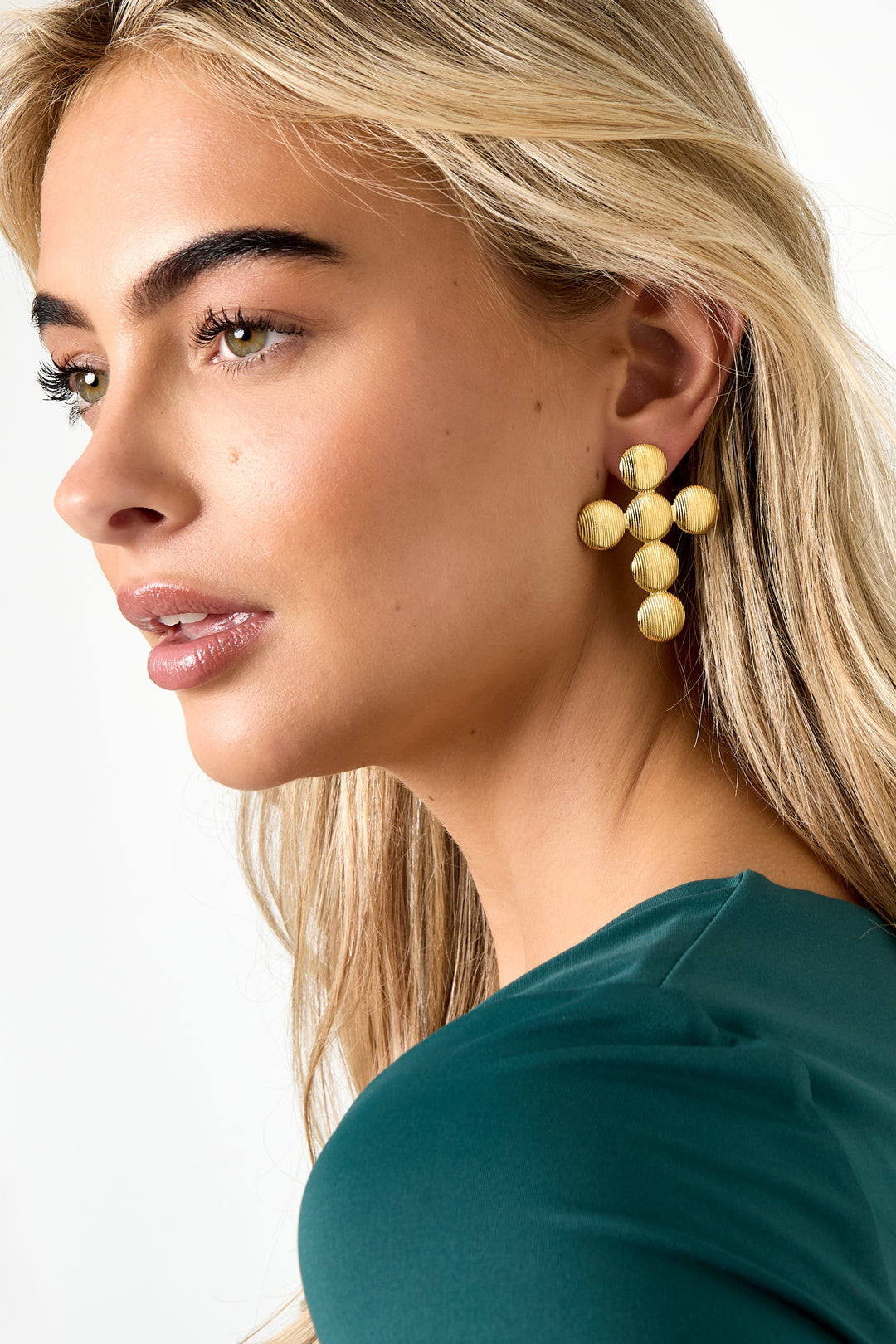 Close-up side profile of a woman wearing large textured gold cross stud earrings with ribbed surface accentuating the design