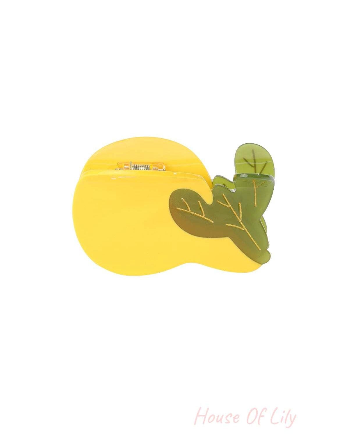 Close-up of yellow pear-shaped hair claw with green leaves detail against white background