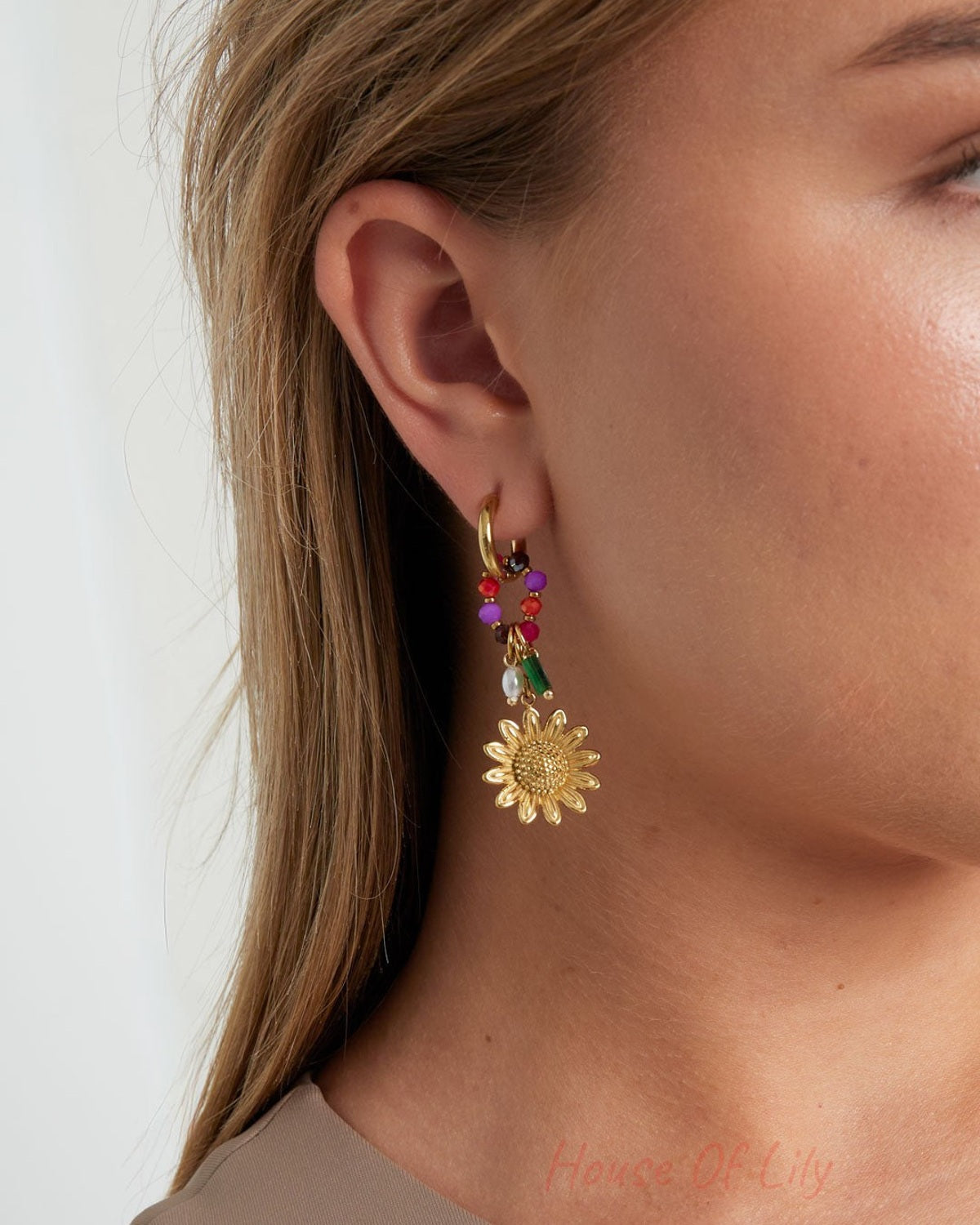 Close-up of a woman wearing gold sunflower charm hoop earrings with colorful beads showing details and fit