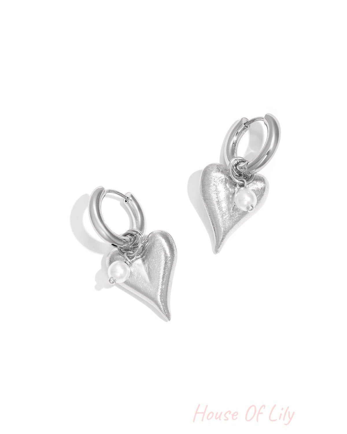 Pair of silver heart charm hoop earrings with pearl detail on white background